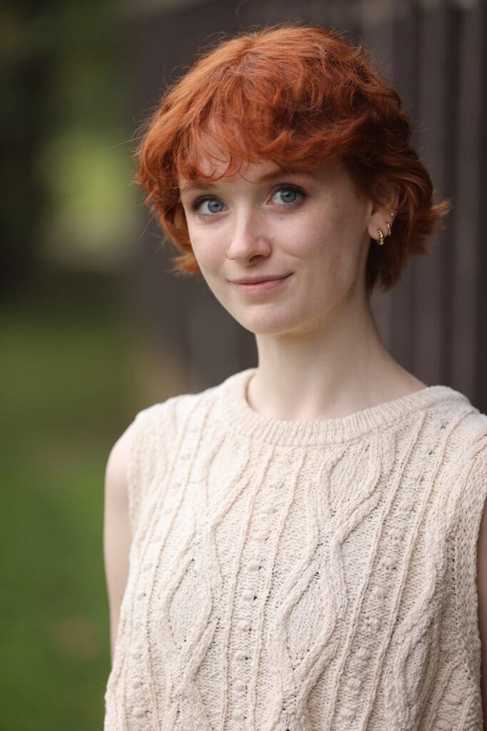 Young woman with red hair wearing a cream cable-knit sweater.